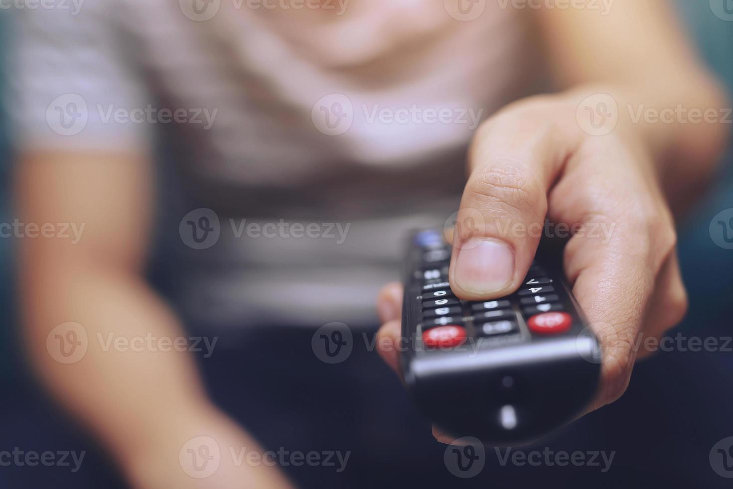 primo piano telecomando della televisione nelle mani dell'uomo casual che puntano al televisore e lo si accende o si spegne. seleziona il canale guardando la tv sul divano di casa in soggiorno rilassati. foto