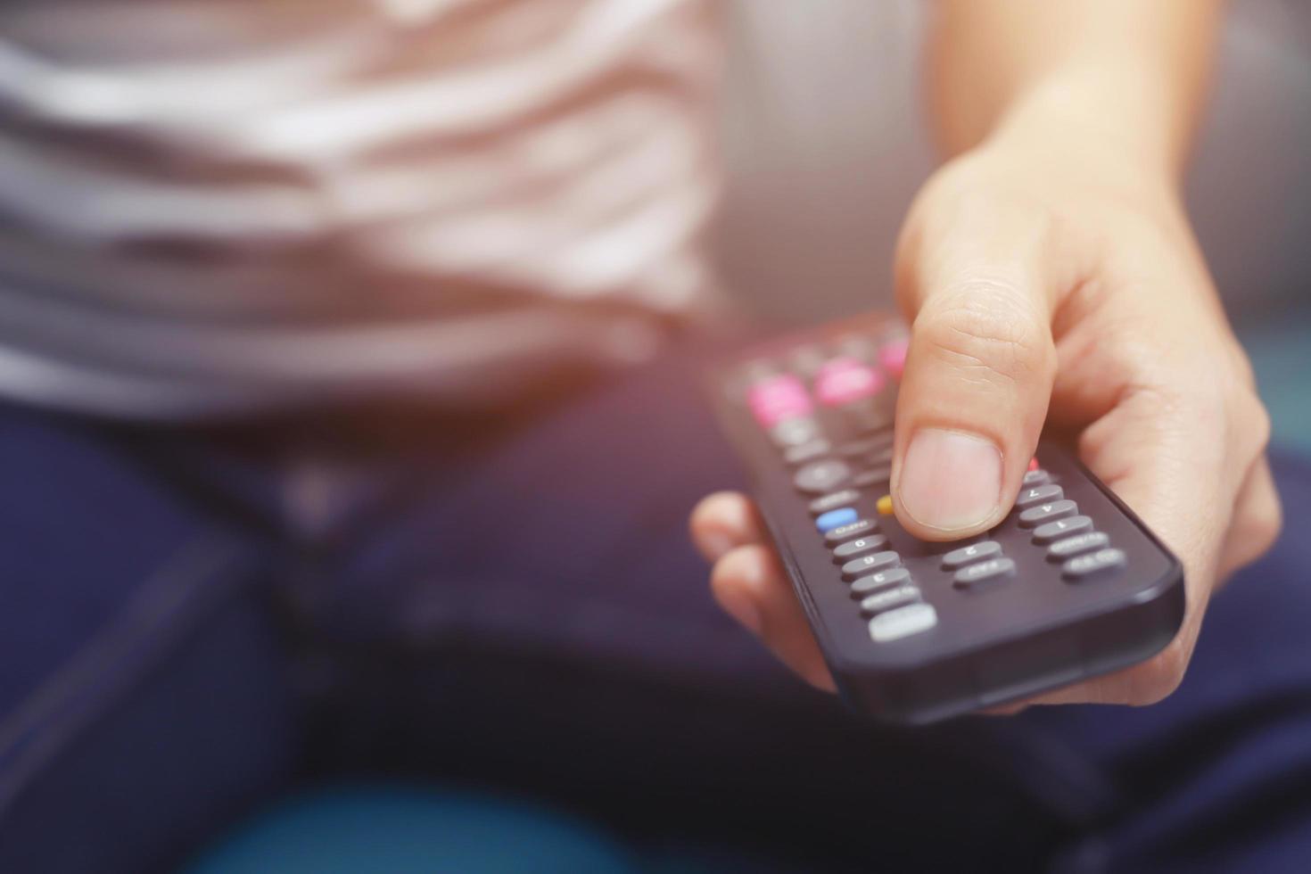 primo piano telecomando della televisione nelle mani dell'uomo casual che puntano al televisore e lo si accende o si spegne. seleziona il canale guardando la tv sul divano di casa in soggiorno rilassati. foto