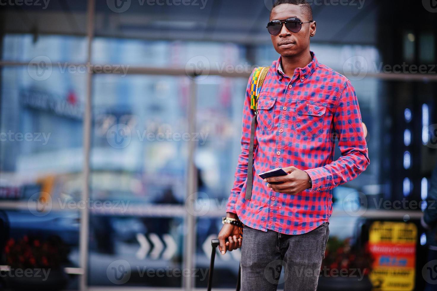 uomo afroamericano in camicia a scacchi, con valigia e zaino. viaggiatore nero contro la stazione degli autobus. foto