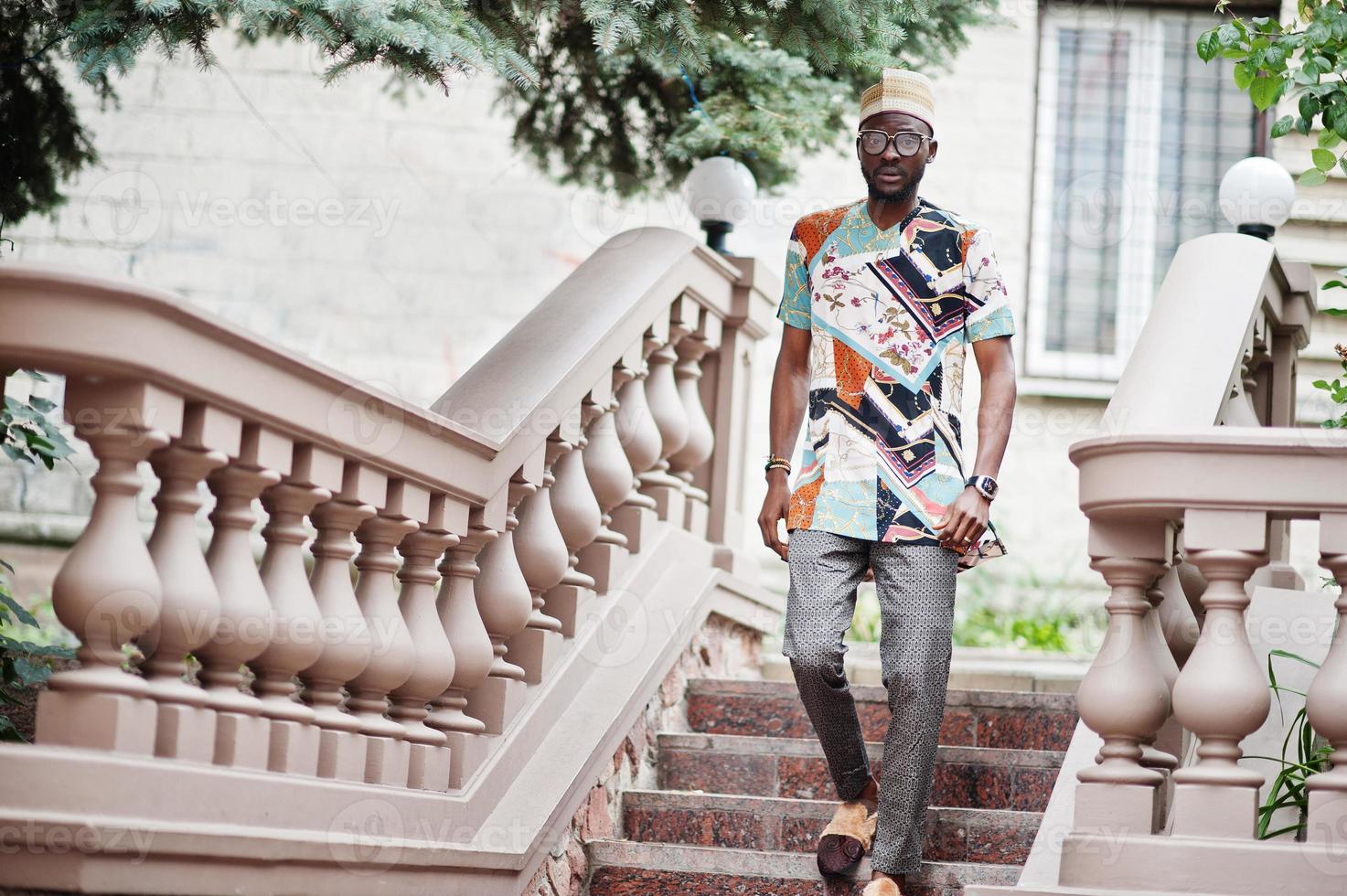 bell'uomo afroamericano che indossa abiti tradizionali, berretto e occhiali nella città moderna. foto