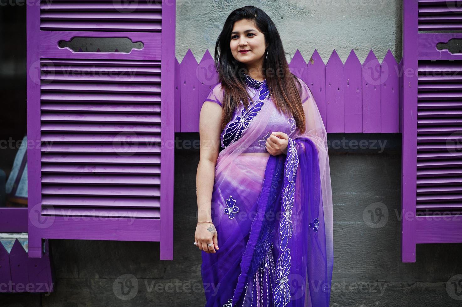 ragazza indù indiana al tradizionale saree viola poste in strada contro le finestre viola. foto