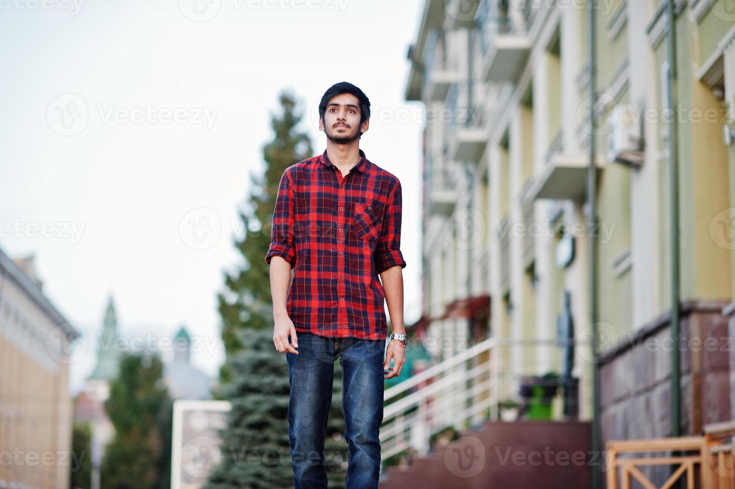 giovane studente indiano in camicia a scacchi rossa e jeans che camminano in città. foto