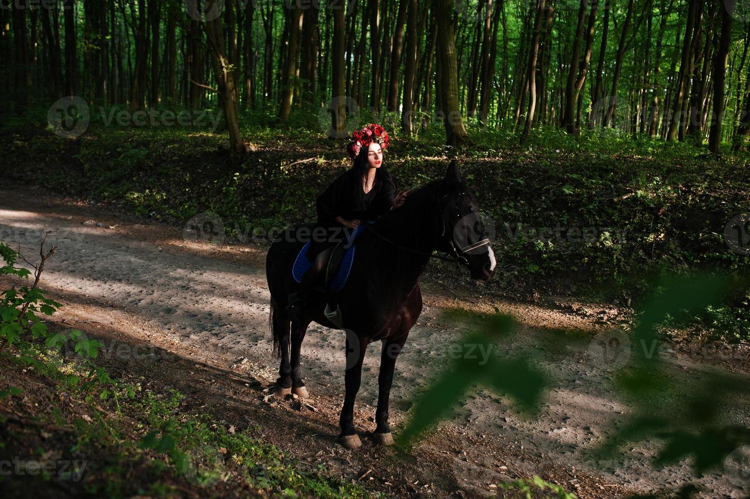 ragazza mistica in ghirlanda indossata in nero a cavallo in legno. foto