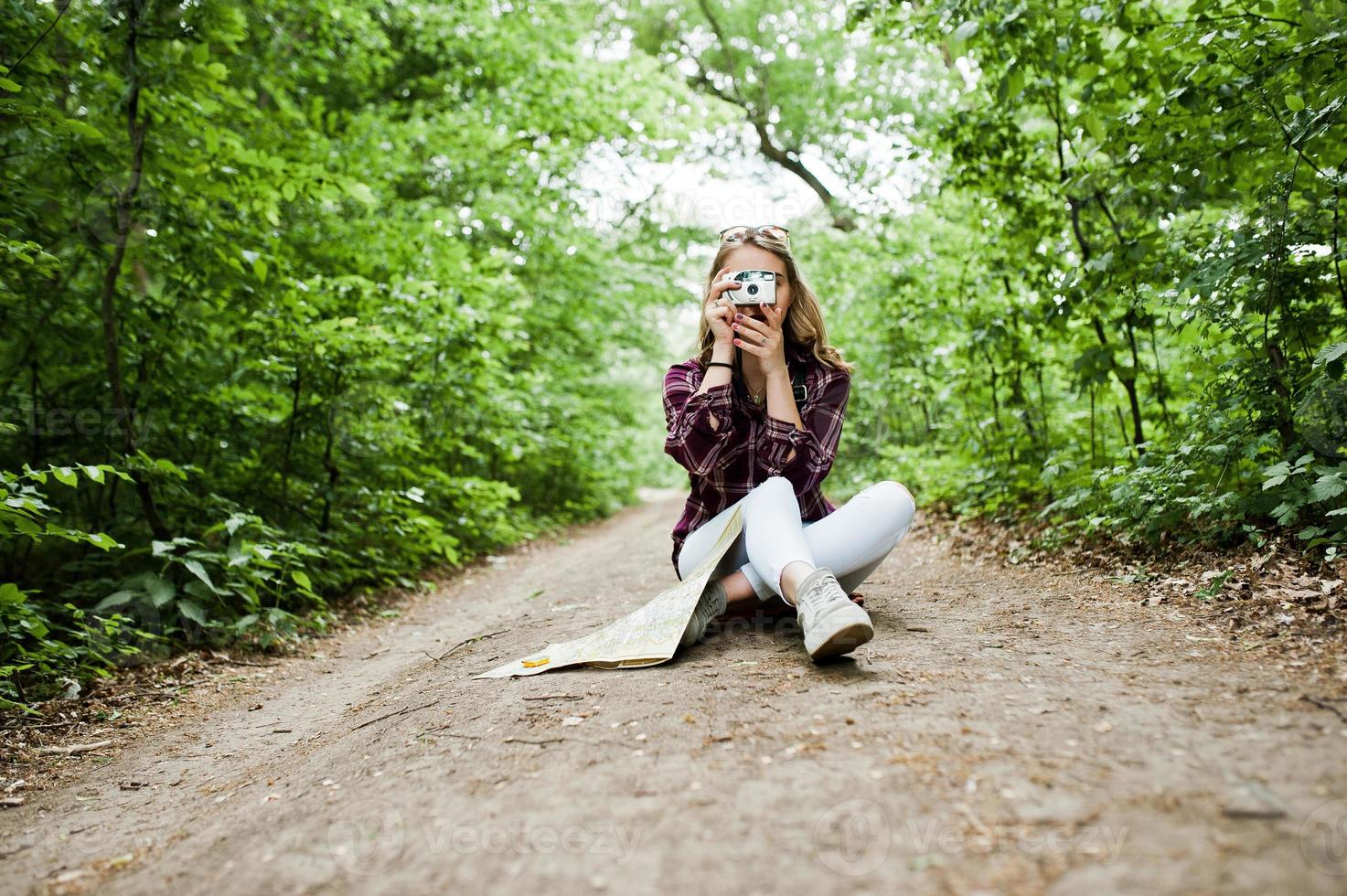 ritratto di una ragazza bionda attraente con una mappa seduta nella foresta e scattare foto. foto