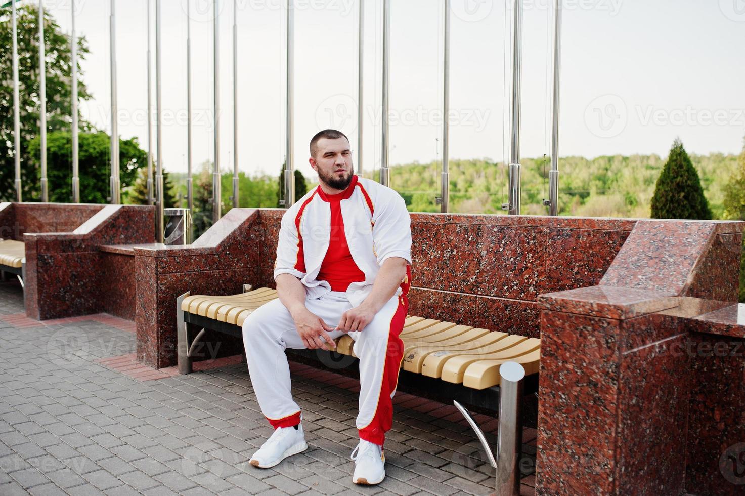 giovane uomo muscoloso barbuto brutale indossa una tuta sportiva bianca con camicia rossa. foto