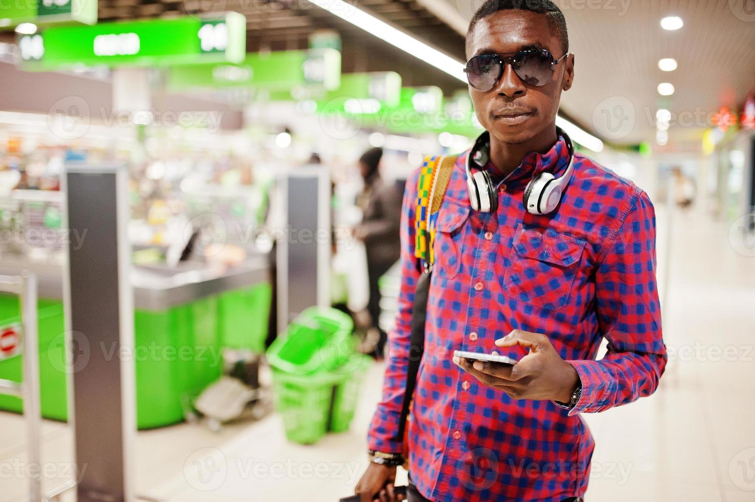 uomo afroamericano in camicia a scacchi con valigia e zaino. uomo di colore contro il supermercato cassiere. foto