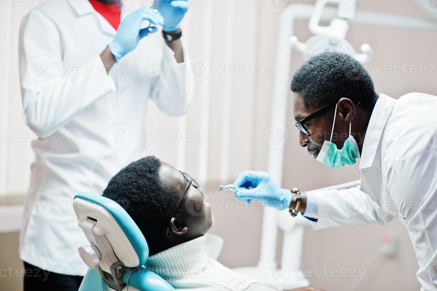 paziente uomo afroamericano in poltrona odontoiatrica. studio dentistico e concetto di pratica medica. dentista professionista che aiuta il suo paziente in odontoiatria medica. perforazione dei denti del paziente in clinica. foto