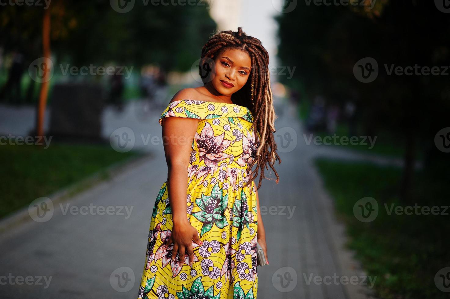 carina ragazza afroamericana di piccola altezza con i dreadlocks, indossa un abito giallo colorato, in posa al tramonto. foto