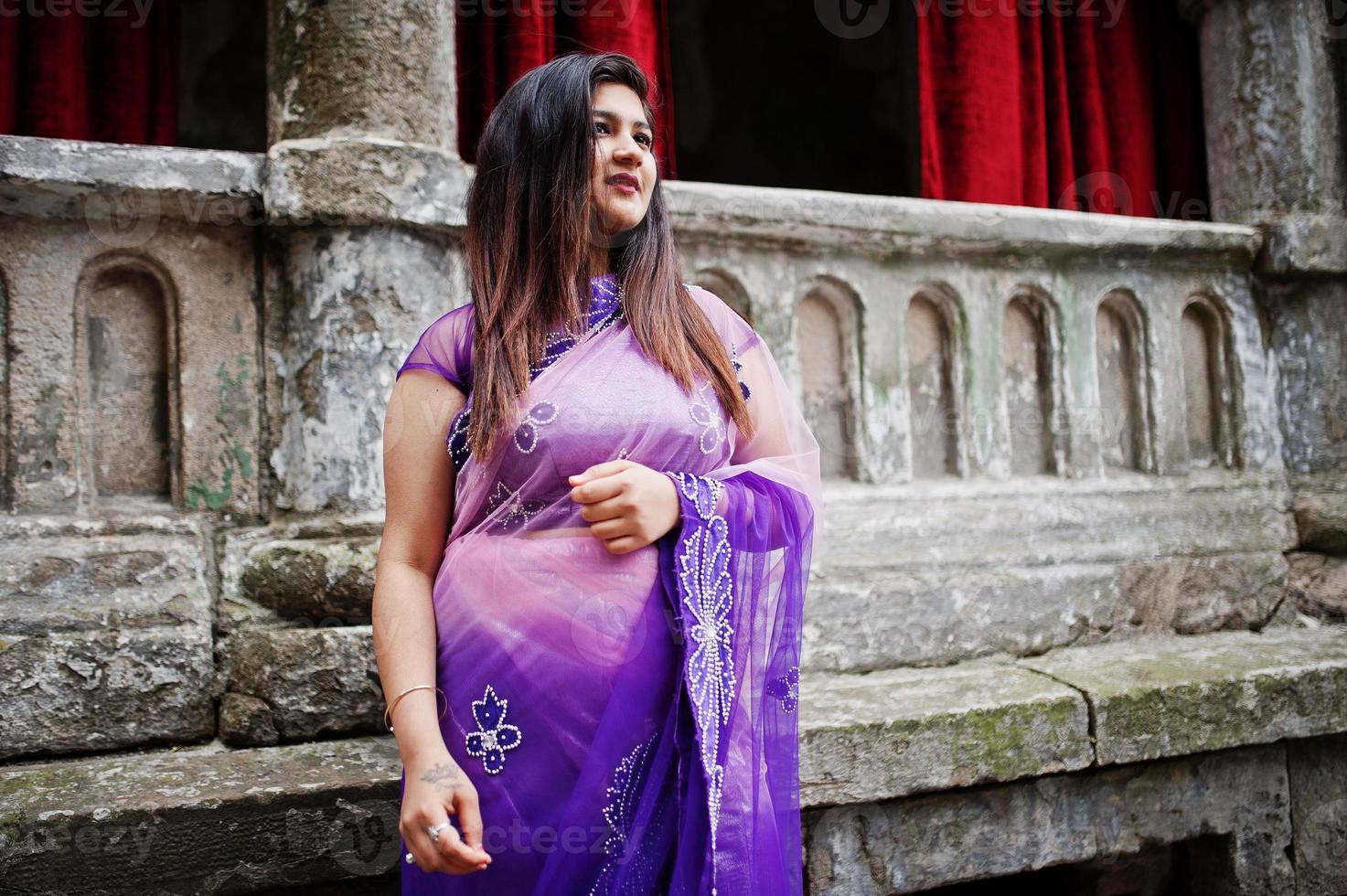 ragazza indù indiana al tradizionale saree viola poste in strada contro la vecchia casa con tende rosse. foto