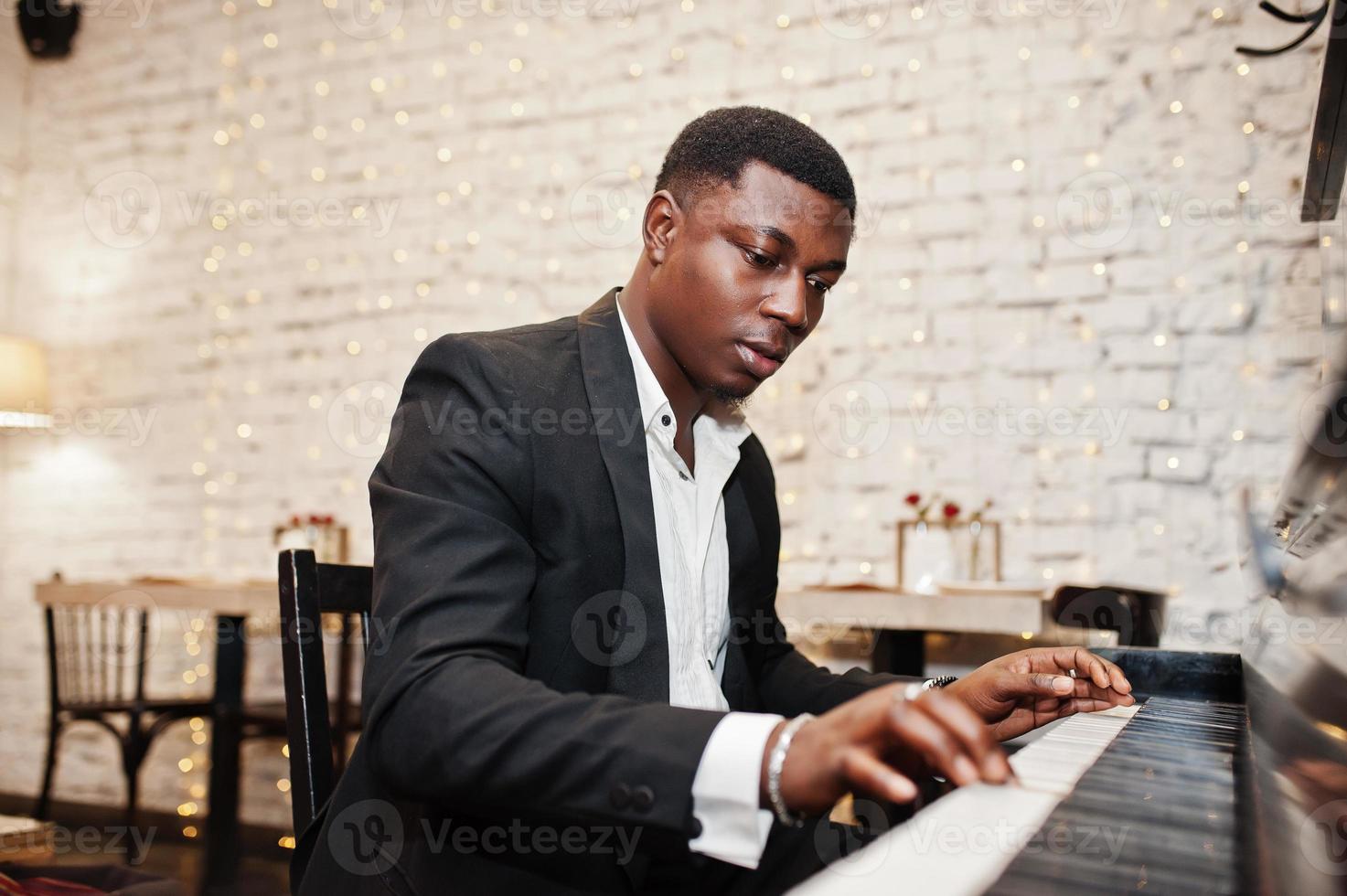 forte e potente uomo afroamericano in abito nero suona il pianoforte. foto