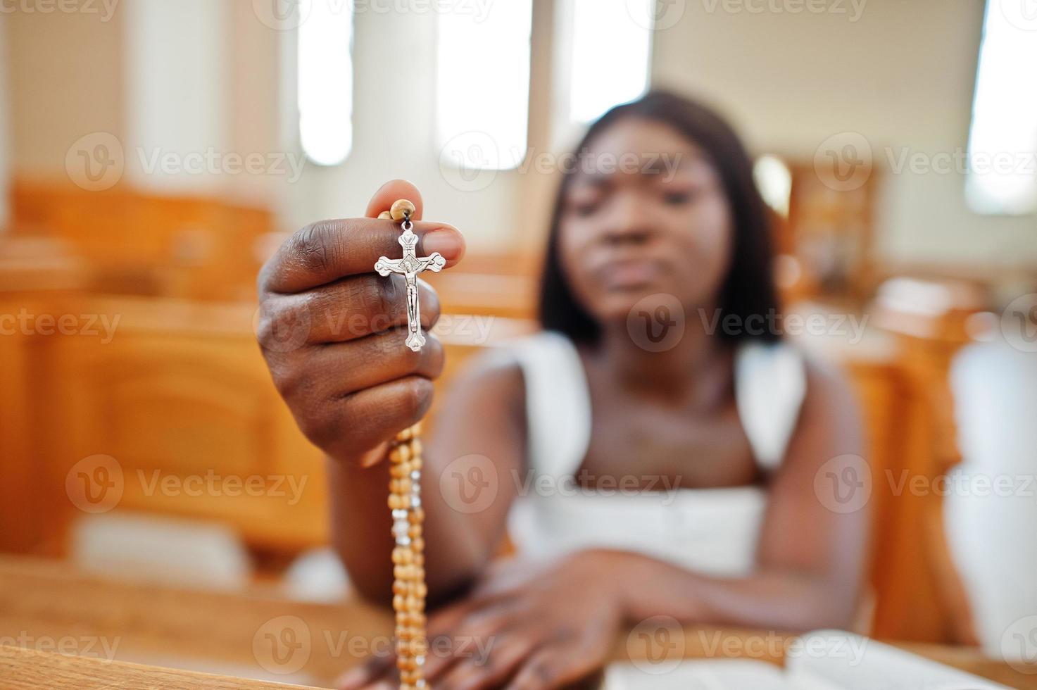 primo piano del rosario a portata di mano. Gesù Cristo croce. donna afroamericana che prega nella chiesa. i credenti meditano nella cattedrale e nel tempo spirituale della preghiera. foto