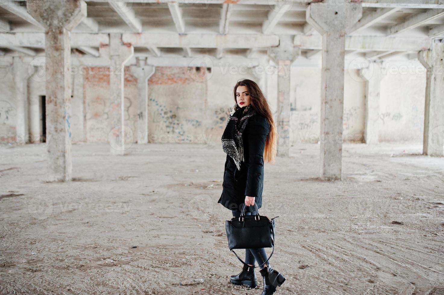 bruna ragazza casual elegante in sciarpa e borsetta contro il luogo di fabbrica abbandonato. foto