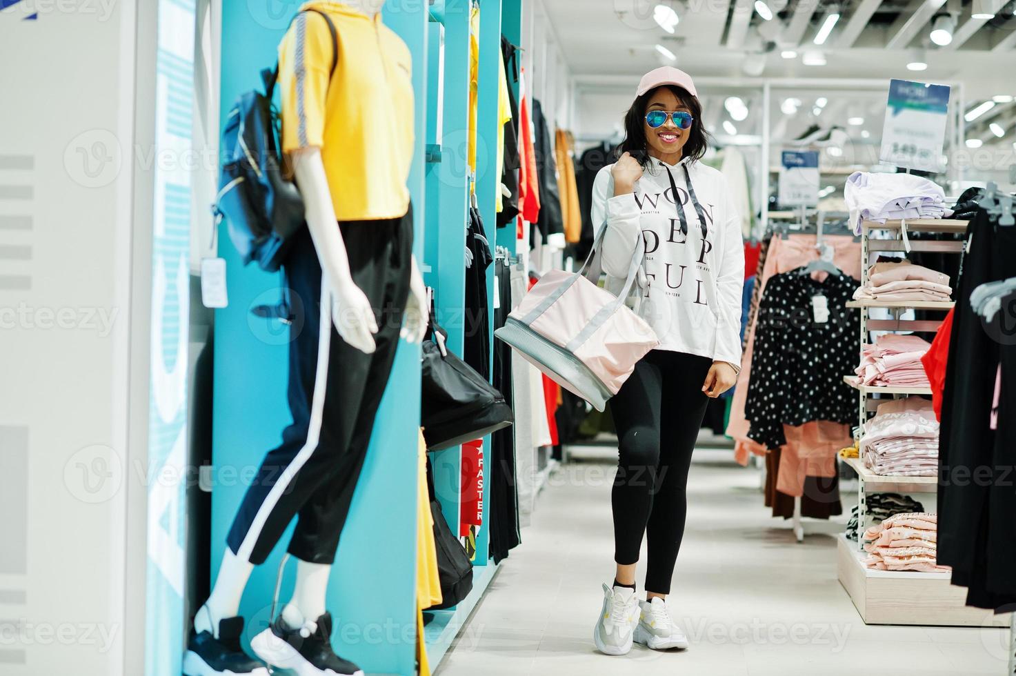 donne americane in tute sportive e occhiali da sole che fanno shopping al centro commerciale di abbigliamento sportivo con borsa sportiva contro scaffali. tema del negozio di sport. foto