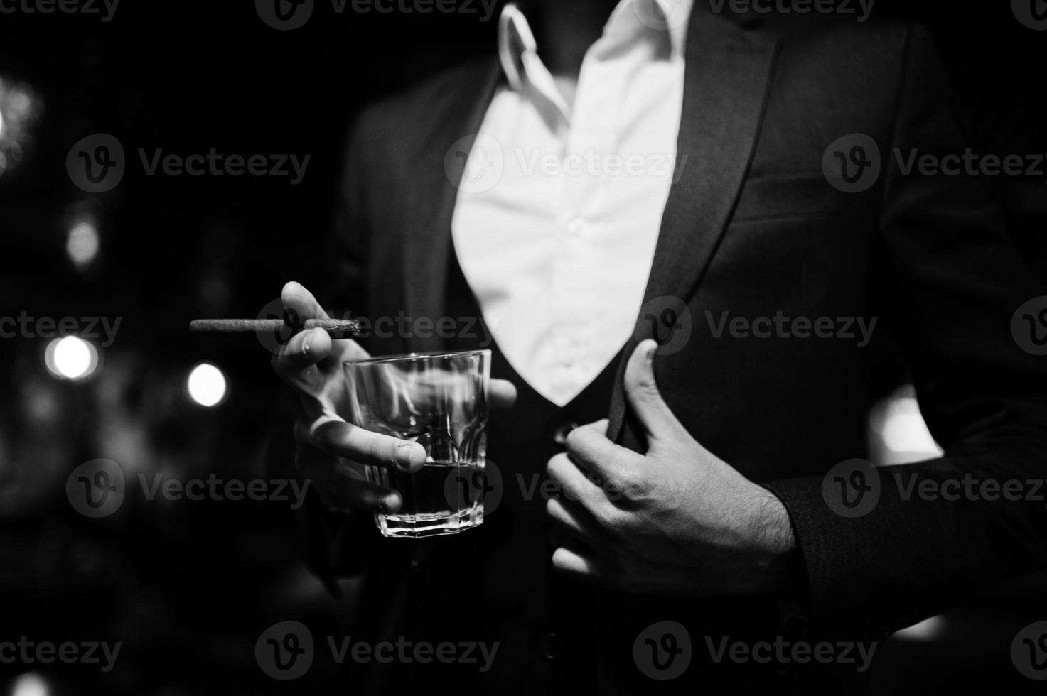 mano ravvicinata di un bell'uomo arabo ben vestito con un bicchiere di whisky e sigaro poste al pub. foto