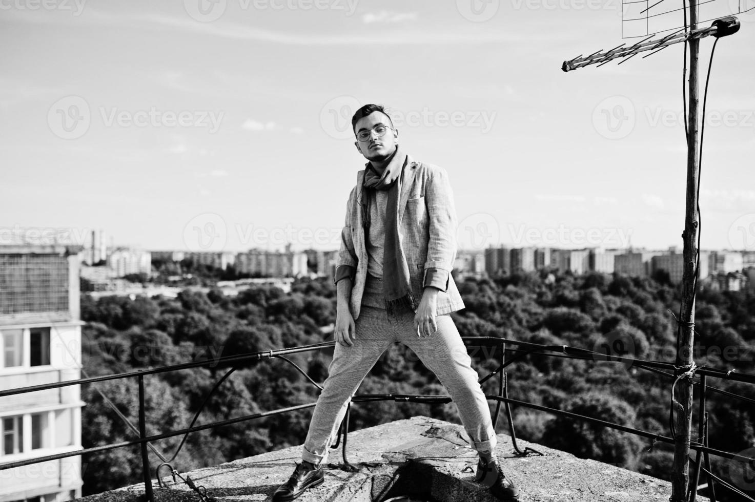 sognatore elegante uomo macho in abito grigio, sciarpa e occhiali posati sul tetto. foto