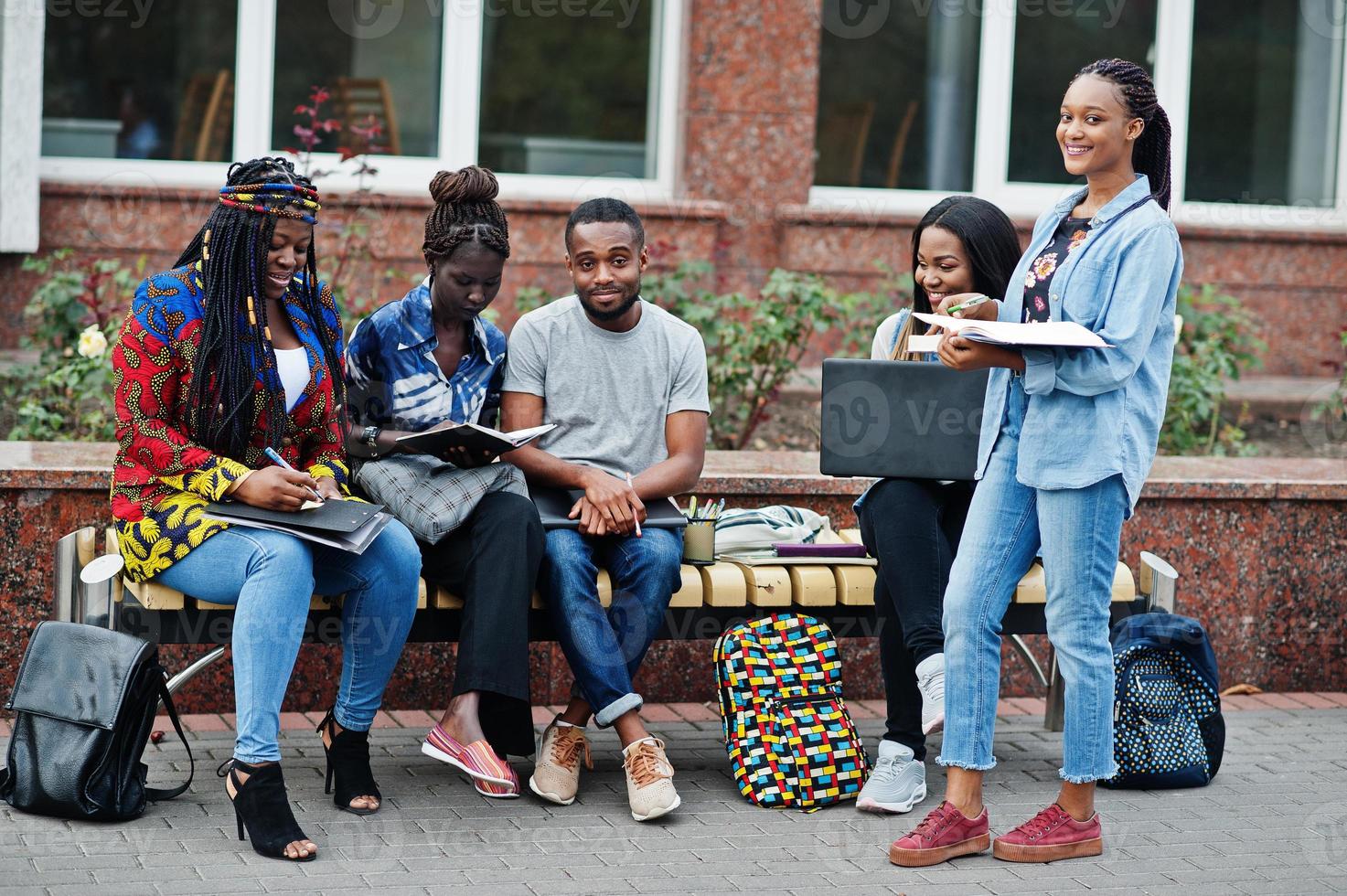 gruppo di cinque studenti universitari africani che trascorrono del tempo insieme nel campus nel cortile dell'università. amici afro neri che studiano al banco con articoli per la scuola, notebook portatili. foto