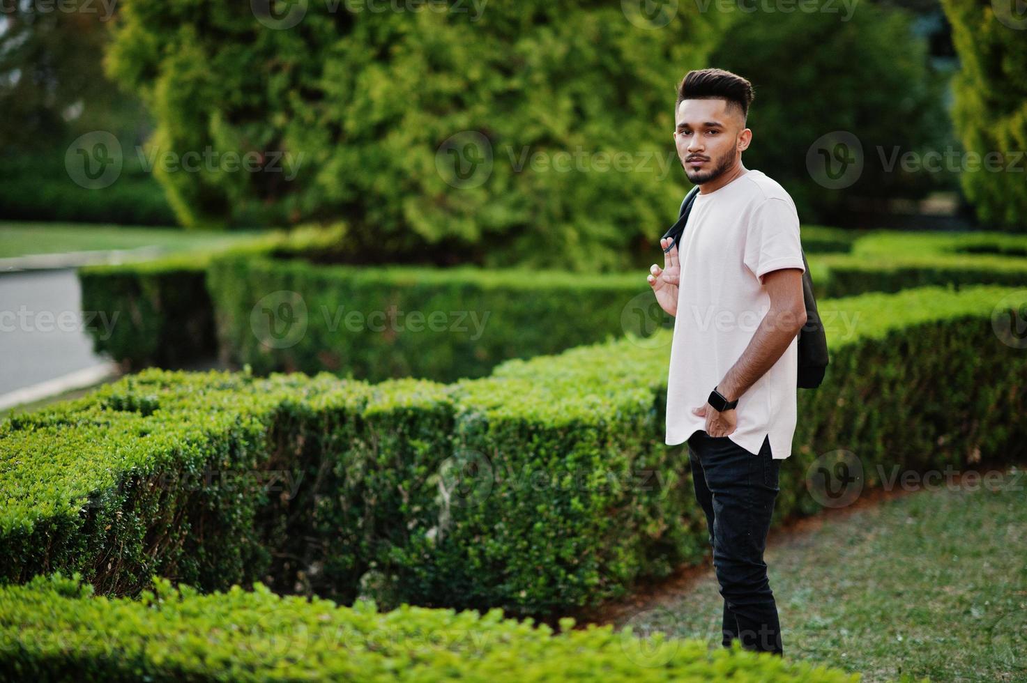 uomo alla moda con barba indiana in giacca di pelle nera. modello indiano posato al giardino verde della città. foto