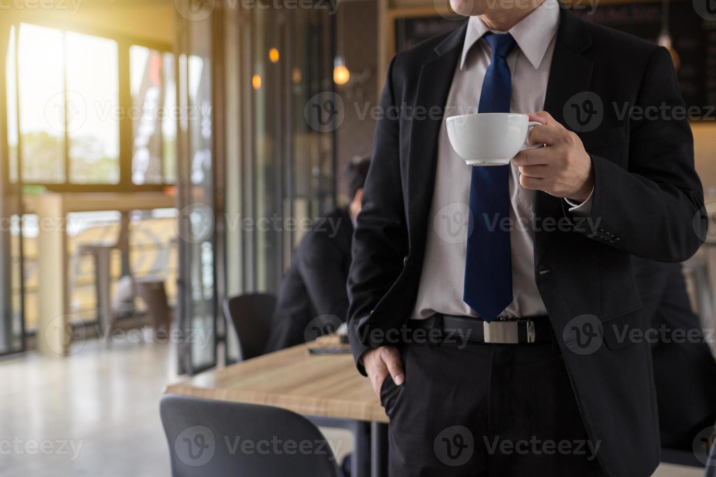 uomo d'affari che tiene una tazza di caffè e distoglie lo sguardo mentre si trova all'aperto con la caffetteria sullo sfondo, riavviando dopo una dura giornata di lavoro. foto
