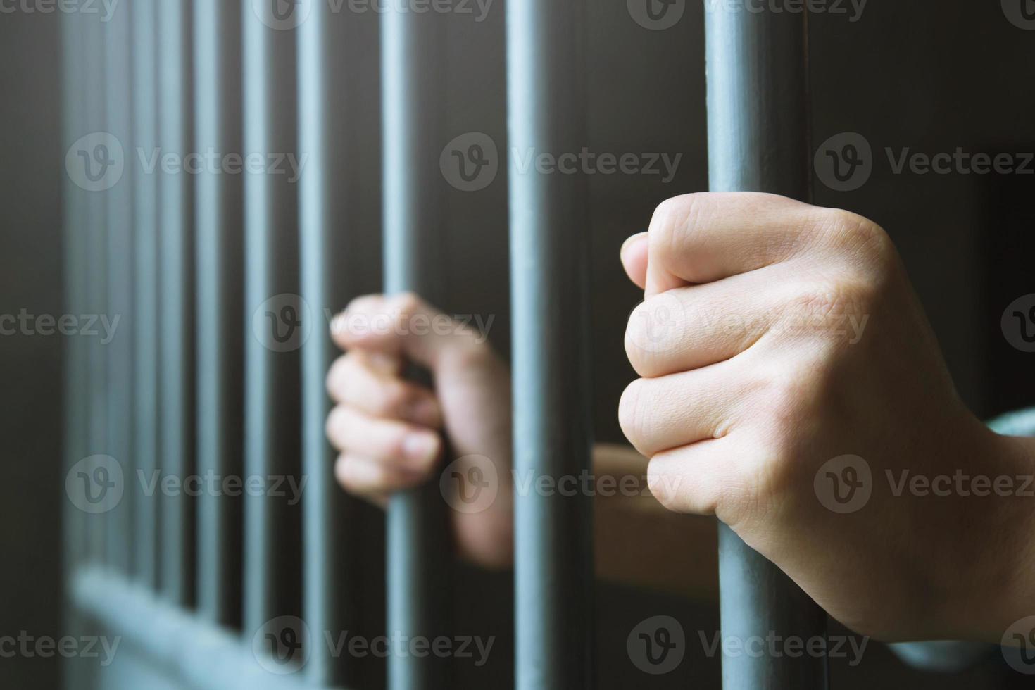 uomo in prigione mani di dietro tenere sbarre di prigione in gabbia d'acciaio. criminale delinquente rinchiuso in carcere. foto