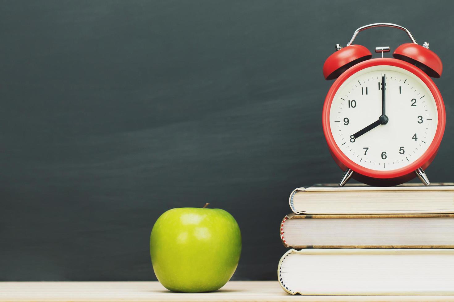 verde mela, sveglia rossa sul libro, messa sullo sfondo della lavagna della cancelleria in legno della scrivania. educazione torna al concetto di scuola. lasciare uno spazio vuoto per la copia del testo. foto