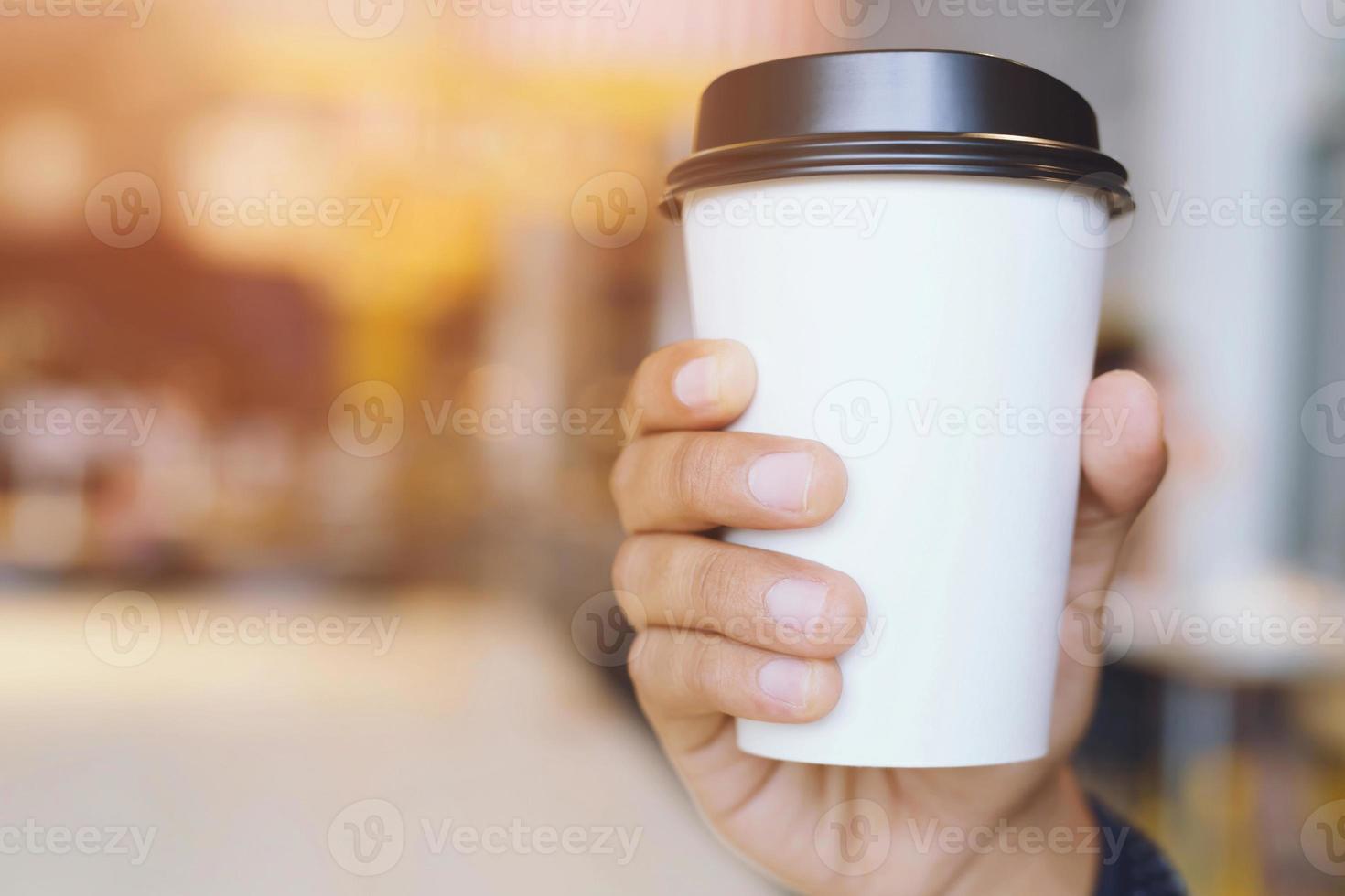 giovane donna mano che tiene tazza di carta da asporto bere caffè caldo sul tavolo in legno nella caffetteria caffetteria. foto