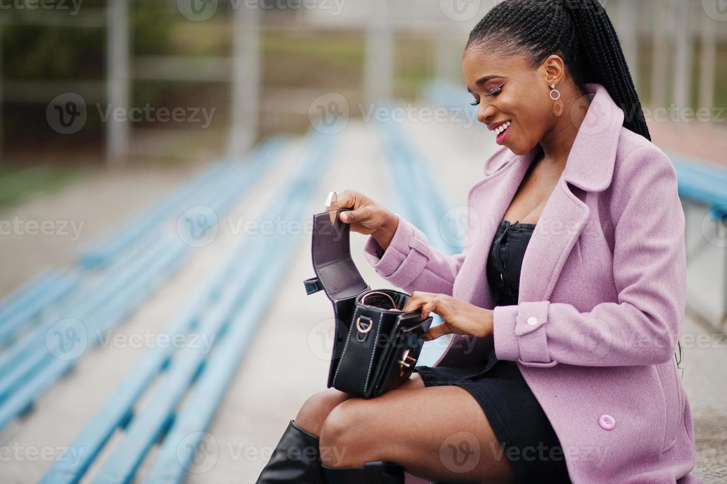 giovane ed elegante bella donna afroamericana in strada alle gradinate dello stadio, indossando un cappotto di moda, con borsetta. foto