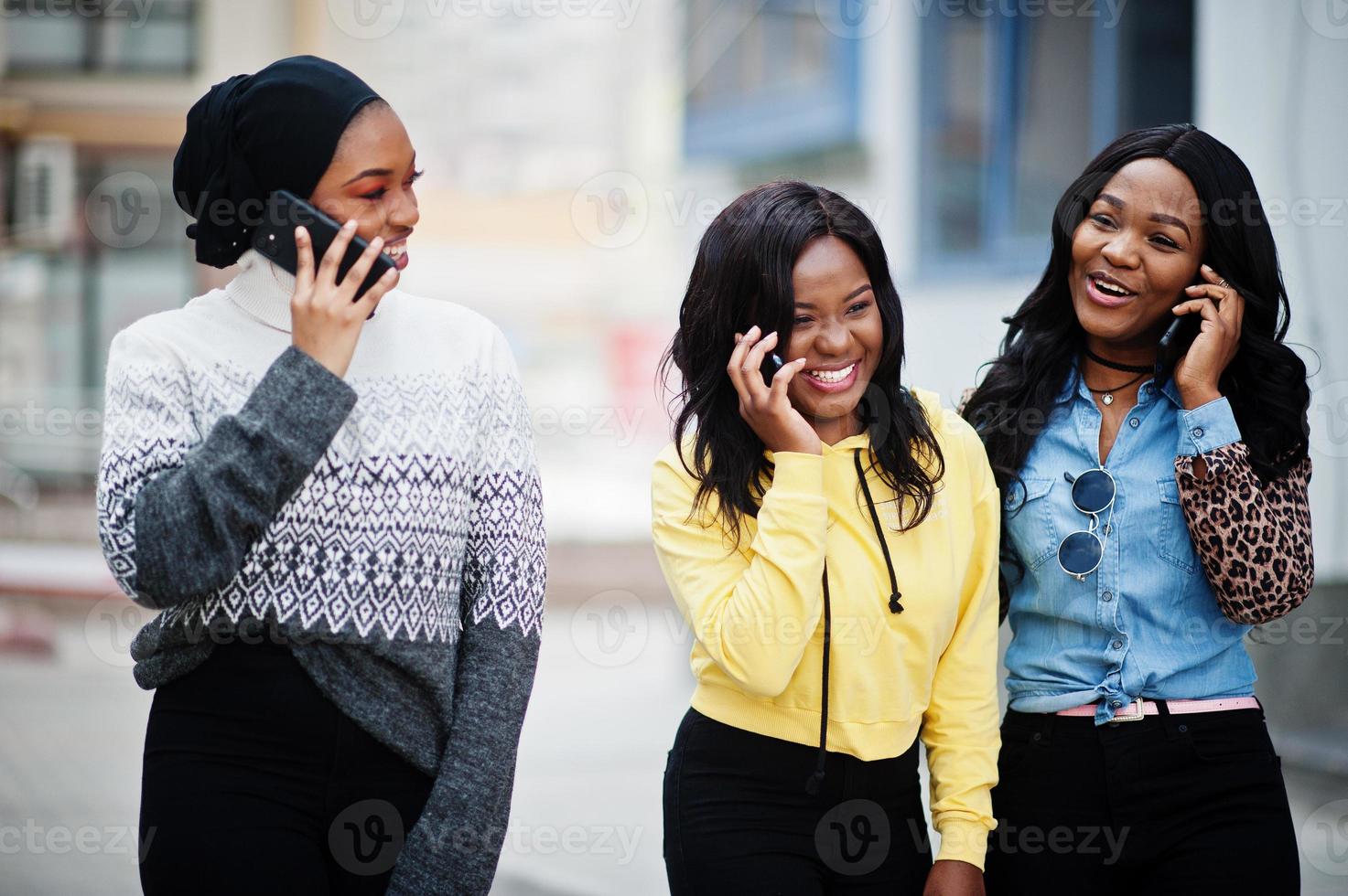 tre giovani amici della donna afroamericana del college con i telefoni cellulari. foto