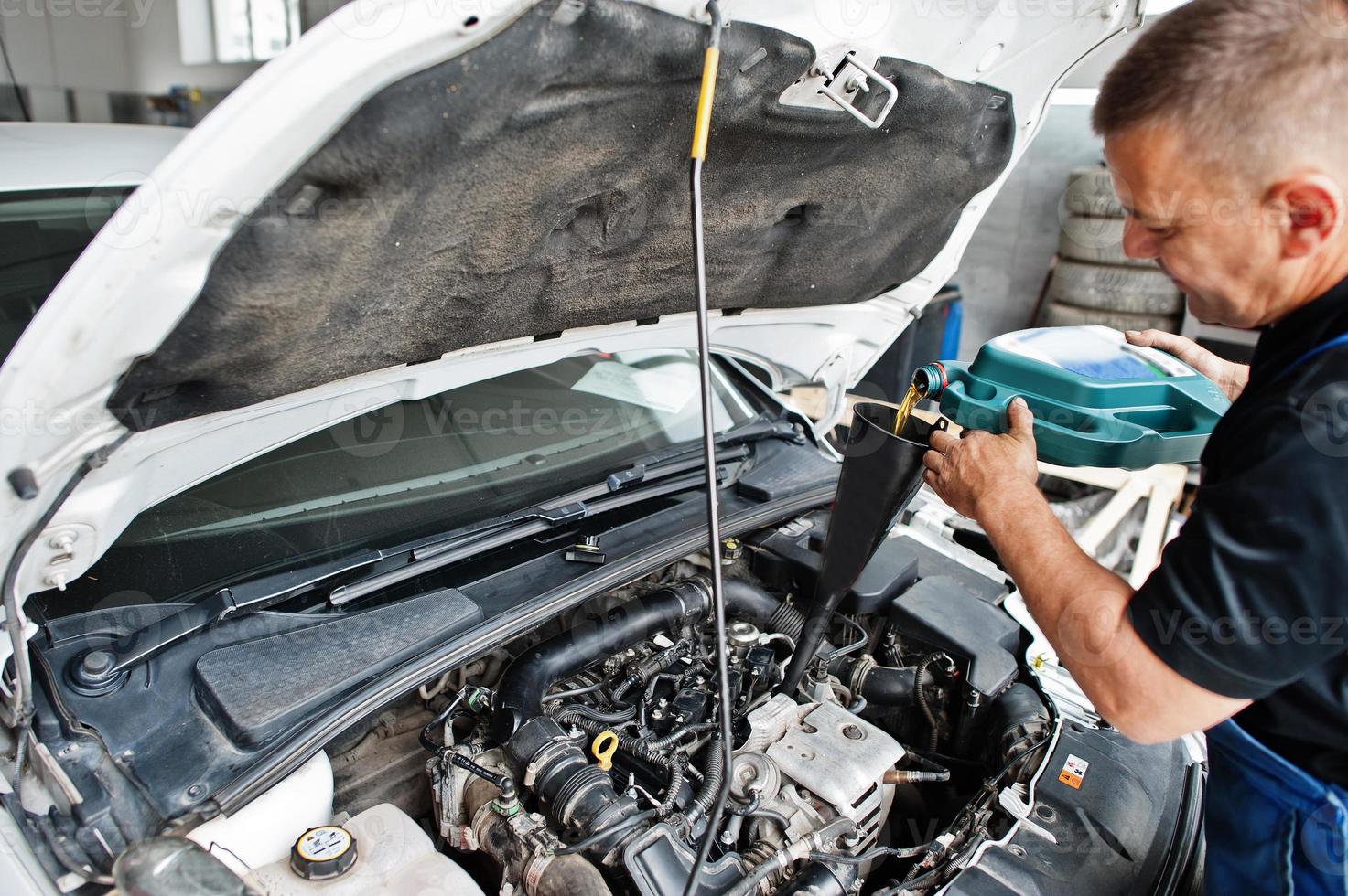 tema riparazione e manutenzione auto. meccanico in uniforme che lavora in servizio auto, versando olio motore nuovo. foto