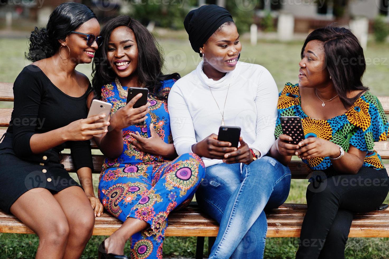 gruppo di quattro ragazze afroamericane sedute su una panchina all'aperto con i telefoni cellulari a portata di mano. foto