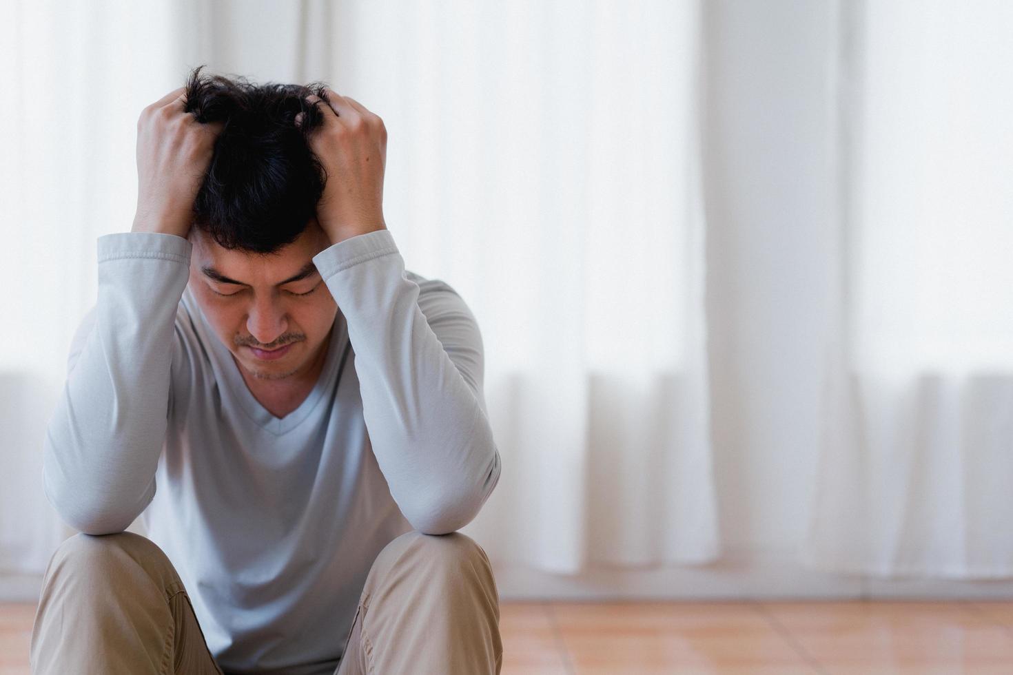 giovane asiatico depresso che copre il viso con le mani, piange da solo a casa, uomo sconvolto seduto, sentirsi infelice dopo una lite o una rottura, disperazione e solitudine e panico, concetto di problema psicologico foto