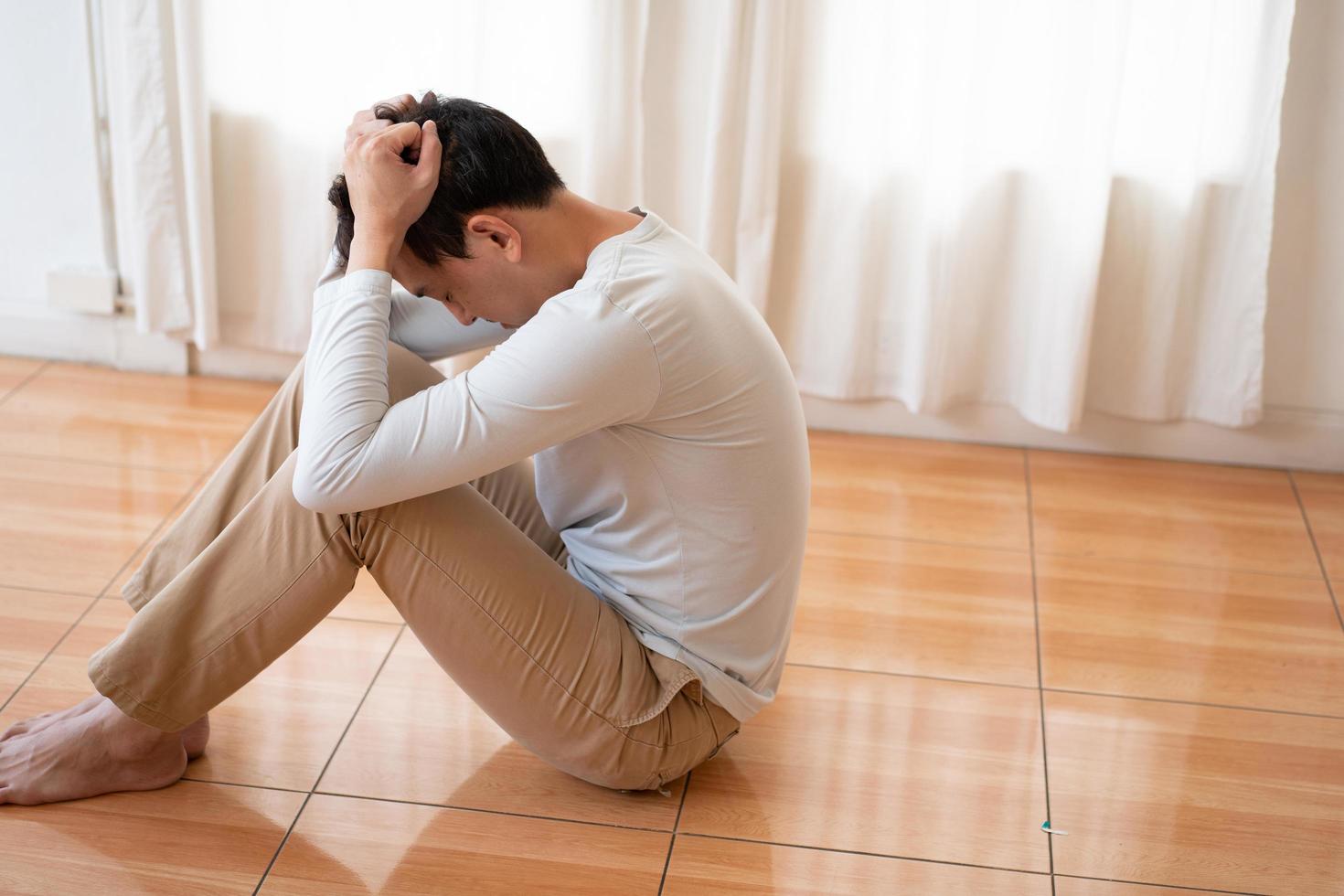 giovane asiatico depresso che copre il viso con le mani, piange da solo a casa, uomo sconvolto seduto, sentirsi infelice dopo una lite o una rottura, disperazione e solitudine e panico, concetto di problema psicologico foto