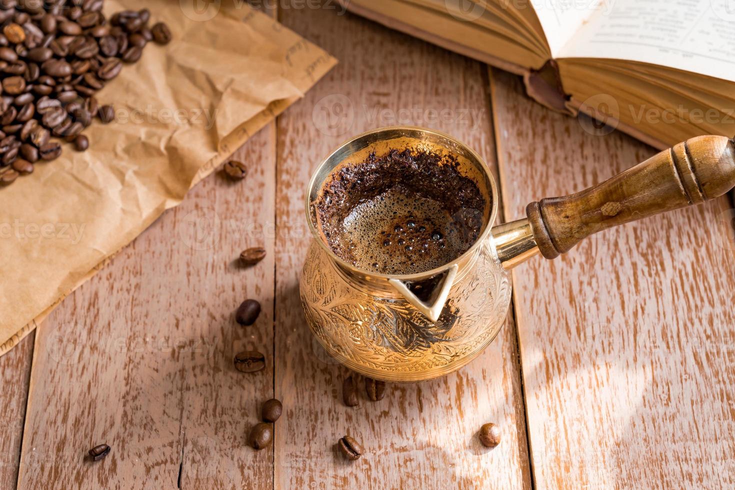 caffè fresco breved in cezve tradizionale caffettiera turca libro aperto e chicchi di caffè sul tavolo di legno. foto