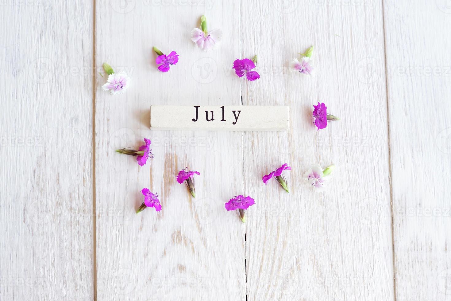 vista dall'alto del calendario in legno con luglio sighn e fiori rosa. foto