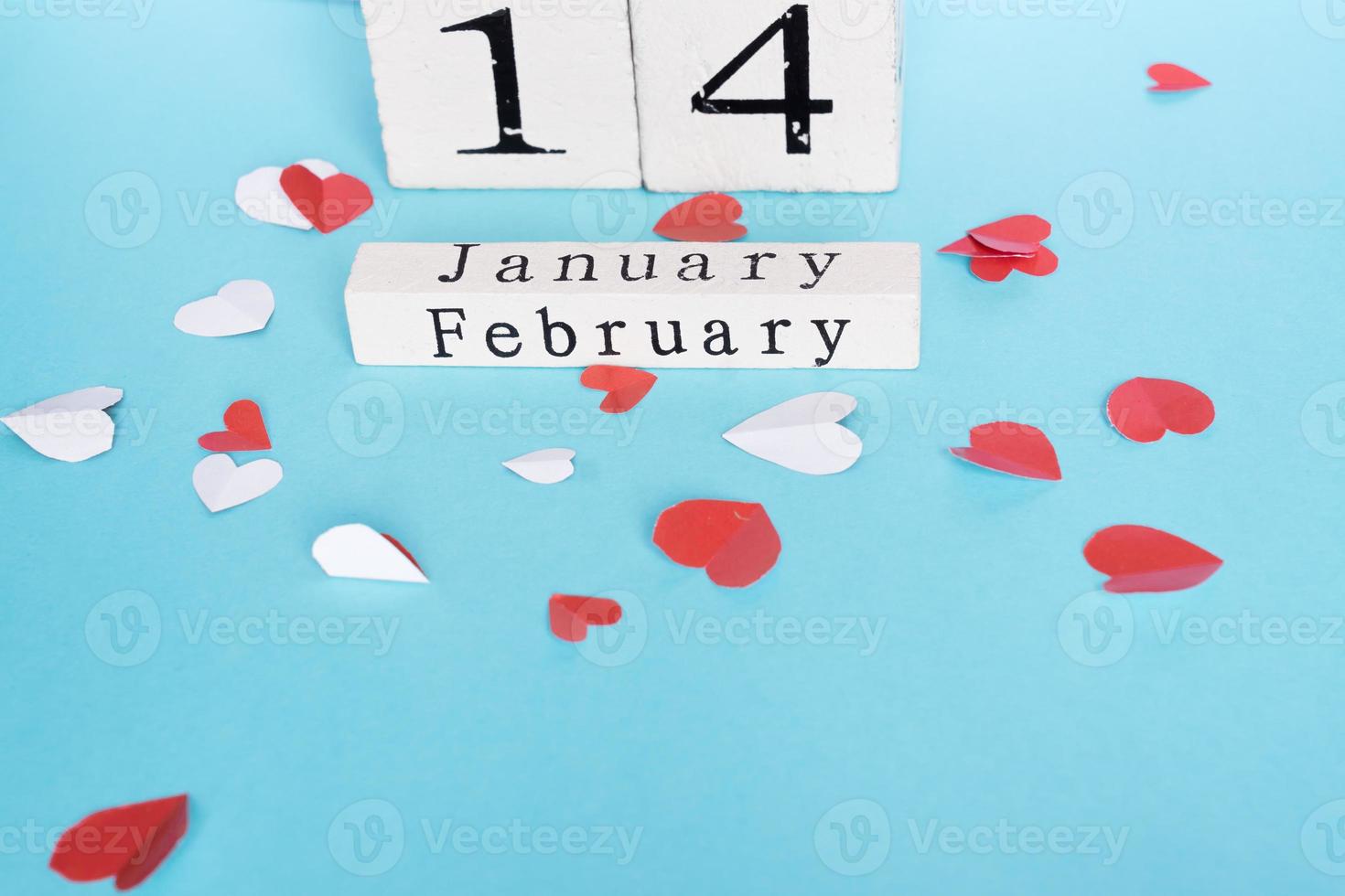 concetto di San Valentino e vacanze - calendario in legno cubo con data del 14 febbraio e cuoricini di carta ritagliati su sfondo blu. decorazione fatta a mano. foto
