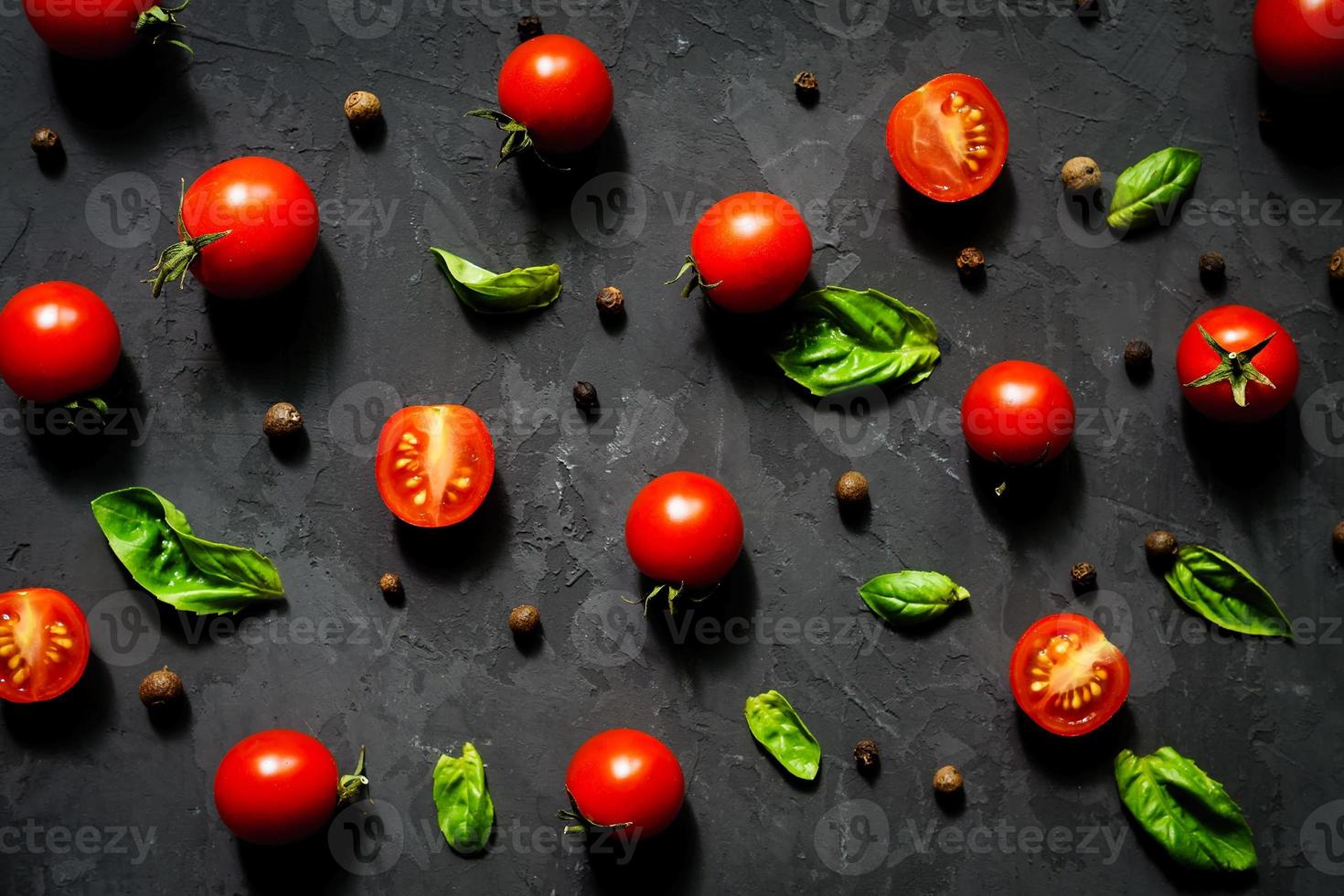 succosi pomodorini tagliati a metà e foglie di basilico su sfondo nero. concetto per una sana alimentazione. vista dall'alto. copia spazio. foto