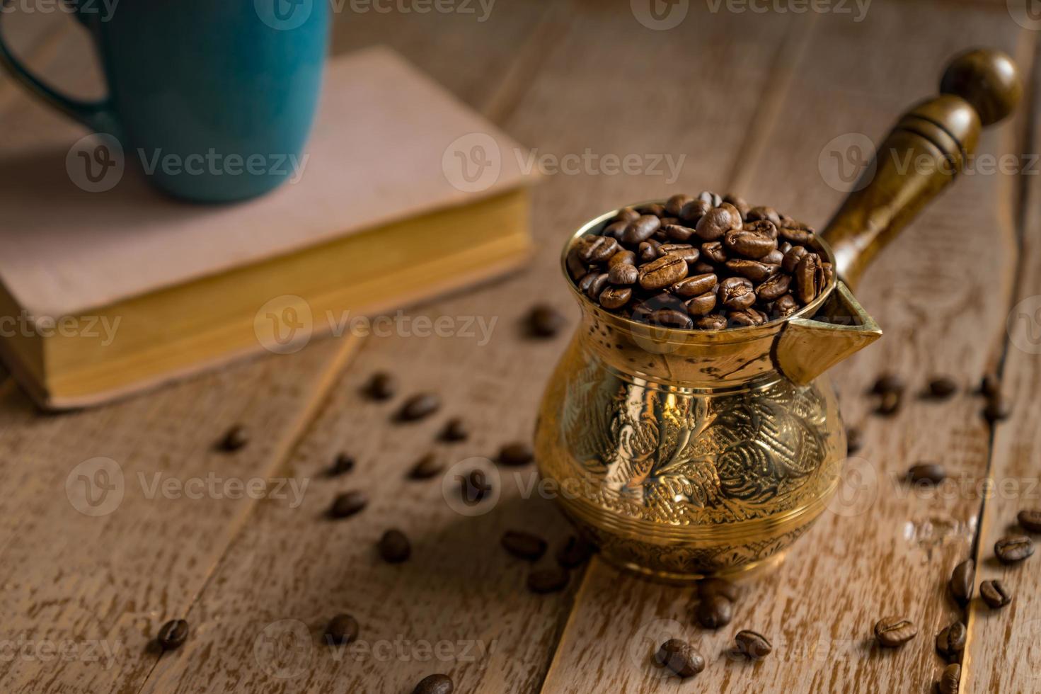 chicchi di caffè tostati freschi in cezve tradizionale caffettiera turca libro chiuso e tazza sul tavolo di legno. foto