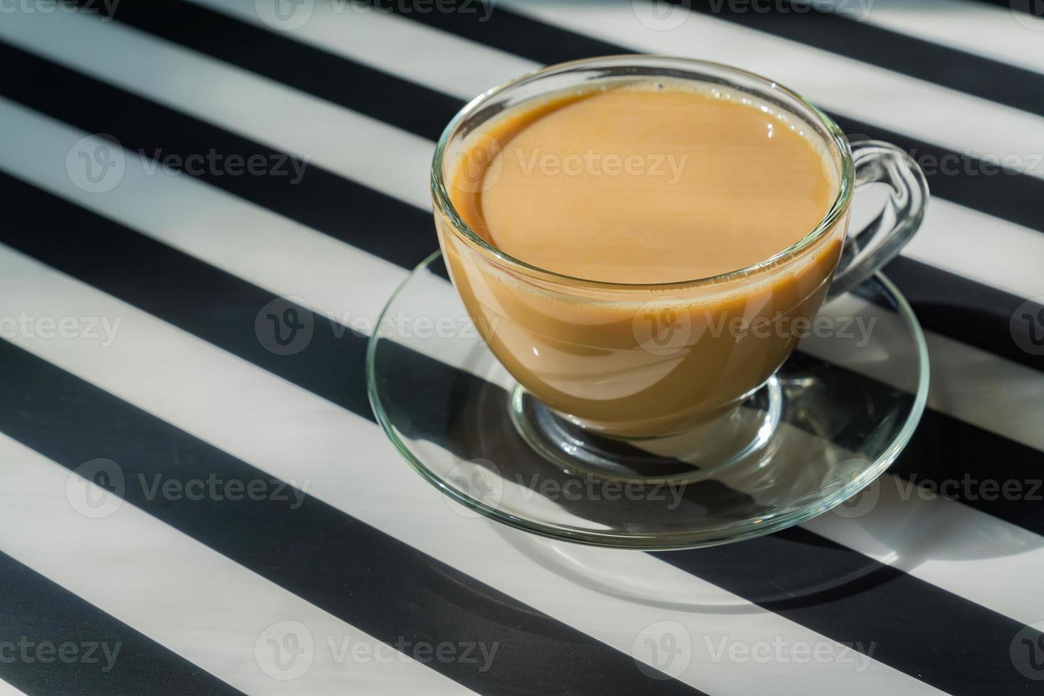 tazza trasparente di caffè cremoso su sfondo scuro. luce solare e ombre dure. immagine dai toni con spazio di copia foto