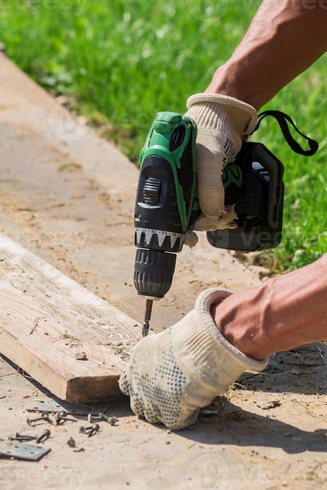 cacciavite elettrico in mano maschile in guanto in tessuto all'aperto. uomo che lavora con uno strumento manuale sul cortile. foto