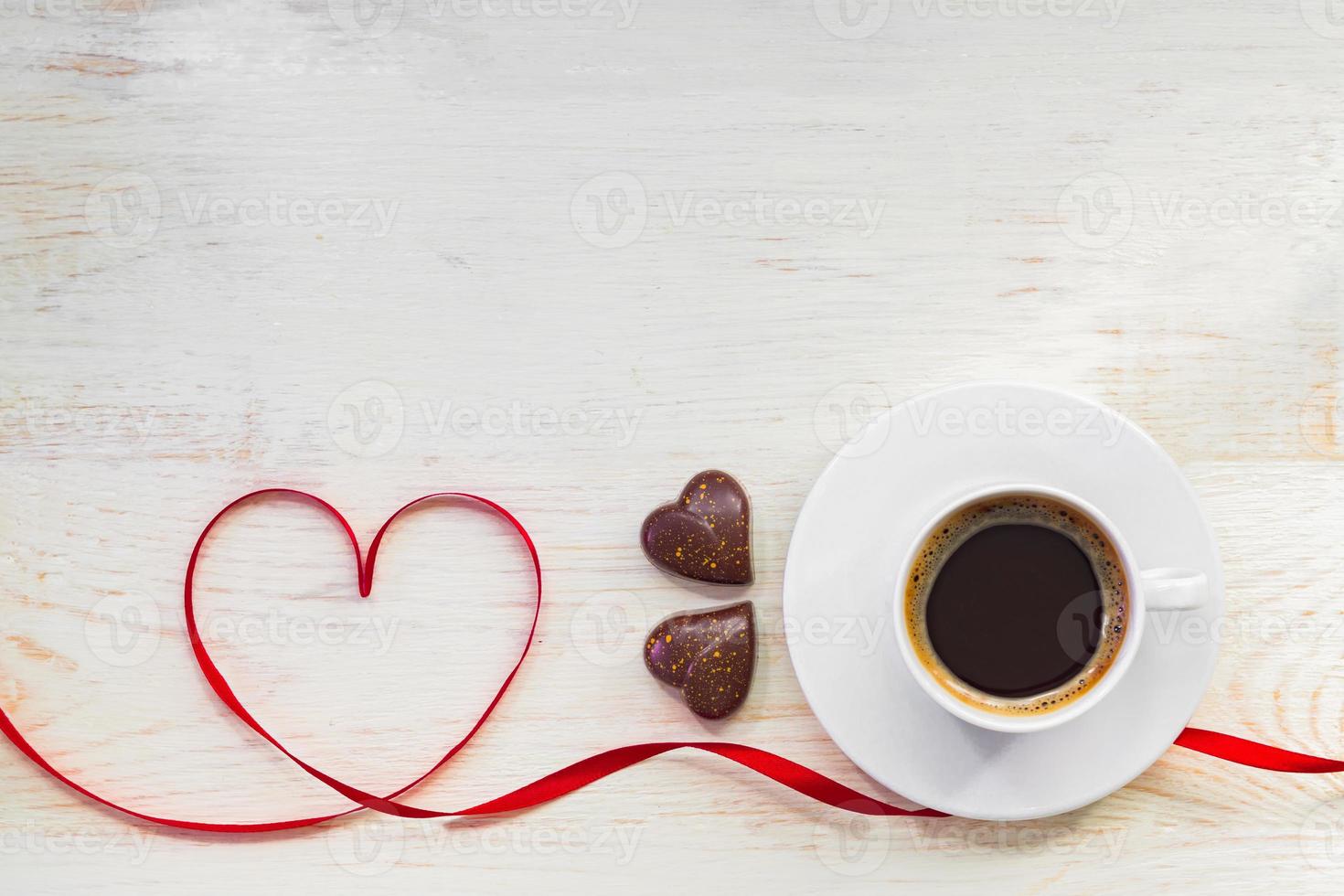 tazza di caffè americano nero con cioccolato placcato oro a forma di cuore e nastro di raso rosso su sfondo di legno. vista dall'alto. copia spazio. biglietto di auguri di San Valentino foto