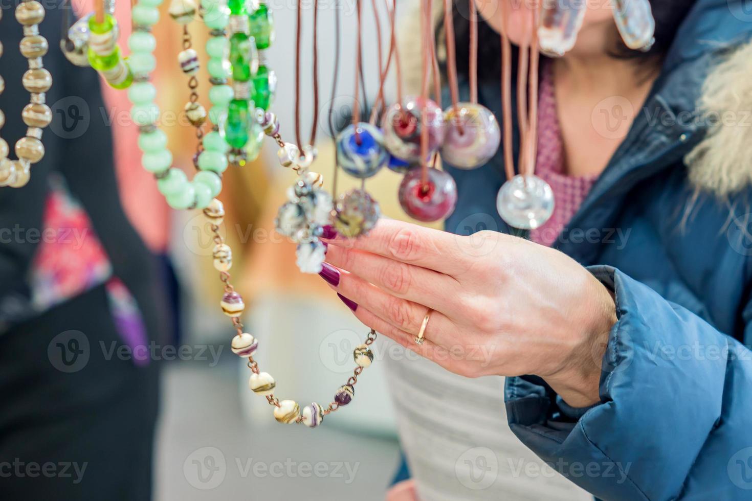 donna bruna in pelliccia blu che sceglie collana sul mercato delle pulci. sfondo dello shopping foto