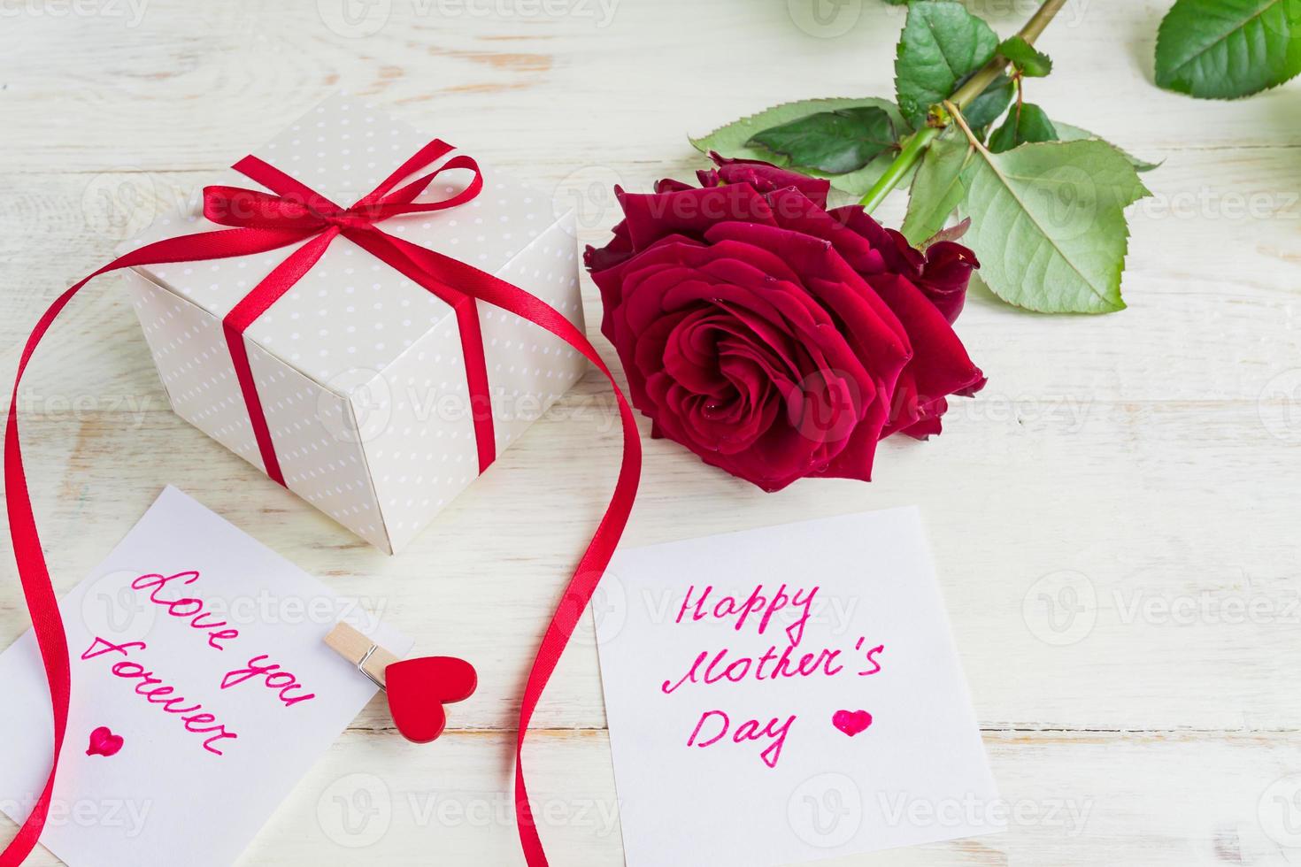 confezione regalo beige a pois con fiocco di nastro rosso e rose rosse bautiful su fondo di legno. biglietto di auguri per la festa della mamma foto