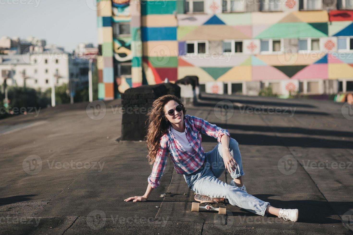 alunno donna nel occhiali da sole e seduta su skateboard foto