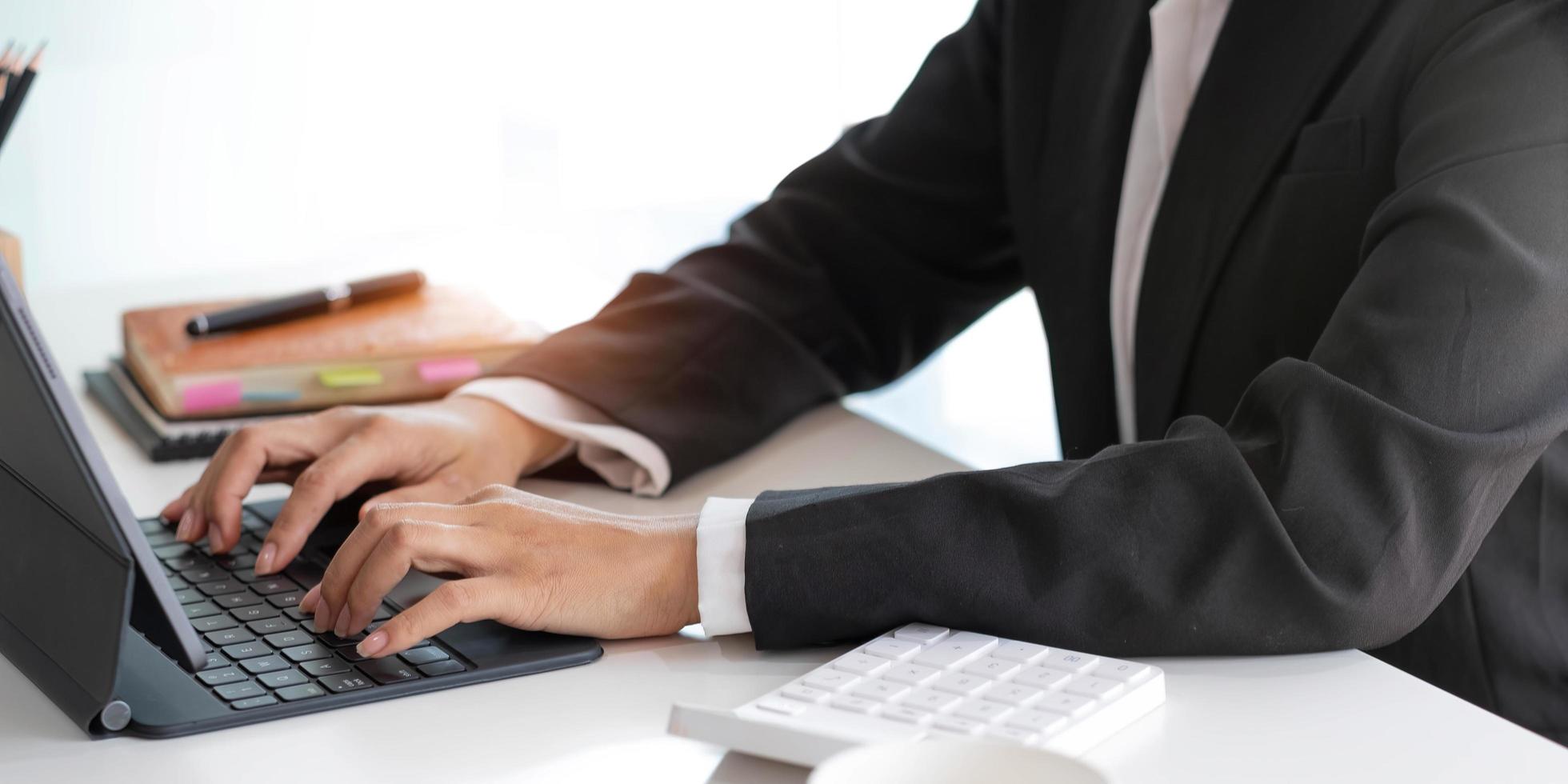 avvicinamento donna di mani opera e digitando su il computer portatile computer con digitale tavoletta su il scrivania a posto di lavoro. foto