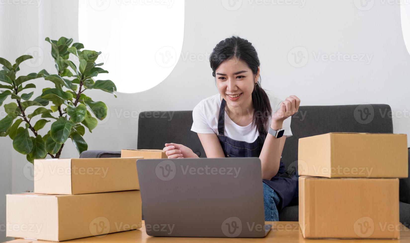 startup piccola impresa imprenditore di freelance donna asiatica che usa un laptop con scatola allegro successo donna asiatica la sua mano alza la scatola di imballaggio di marketing online e consegna sme idea concept foto