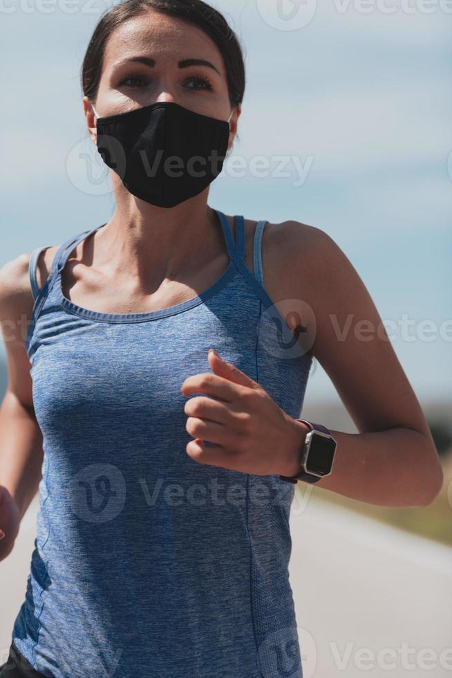 determinato fitness donna nel corto Abiti indossare rosso protettivo viso maschera in esecuzione all'aperto nel il città durante coronavirus scoppio. covid 19 e fisico jogging attività, sport e fitness. foto