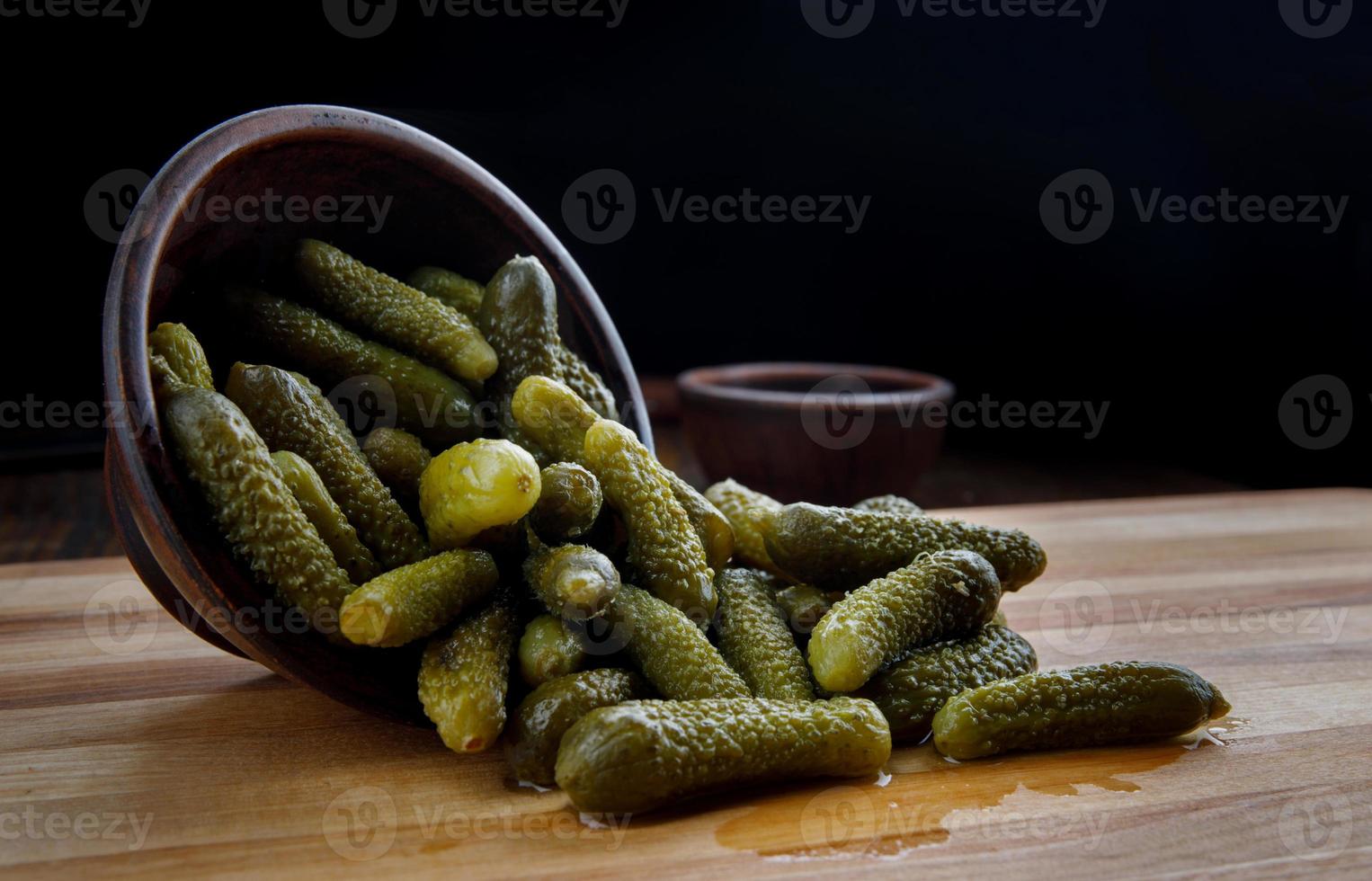 succoso croccante sottaceto cetrioli siamo versato a partire dal un' argilla tazza su un' di legno taglio tavola. salato cetrioli. foto