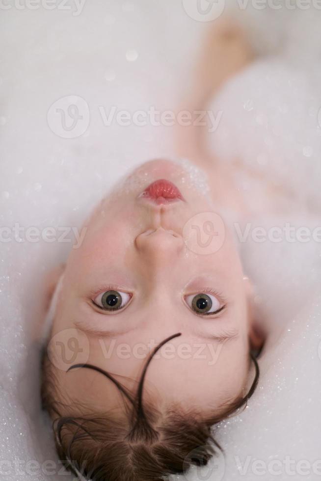 poco ragazza nel bagno giocando con sapone schiuma foto