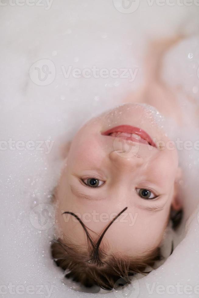poco ragazza nel bagno giocando con sapone schiuma foto