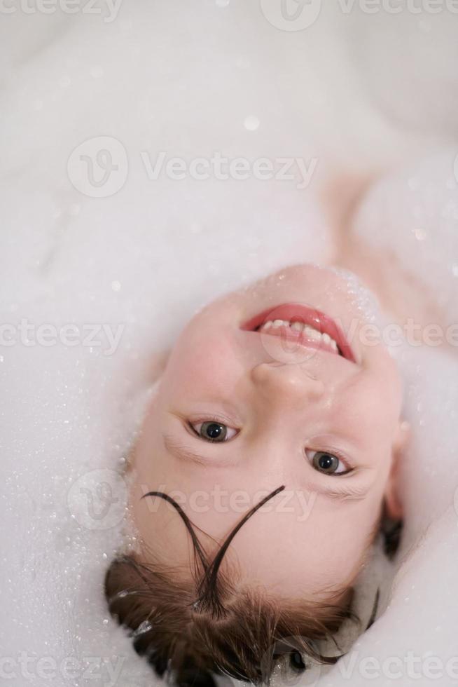 poco ragazza nel bagno giocando con sapone schiuma foto