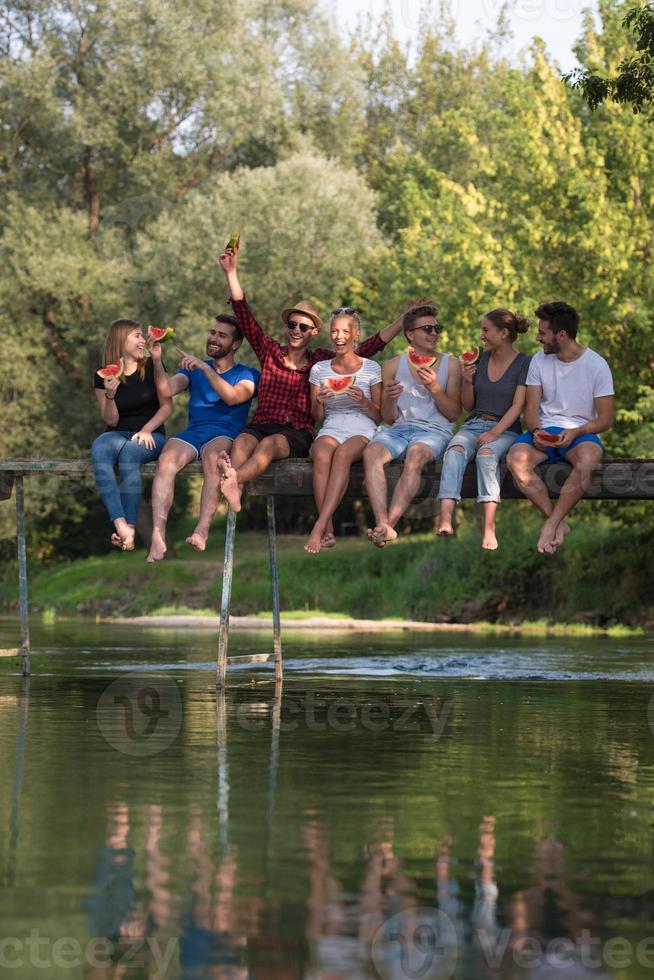 amici godendo anguria mentre seduta su il di legno ponte foto